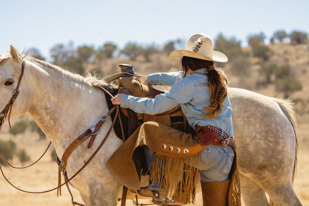 A cowgirl climbing onto a horse.